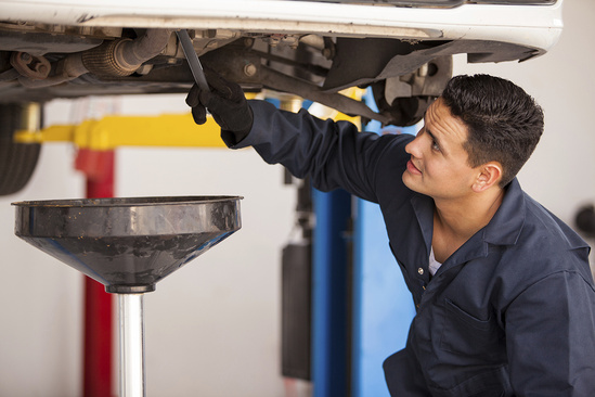 Mechanic performing oil change, checking underneath vehicle with funnel for draining oil in auto repair shop