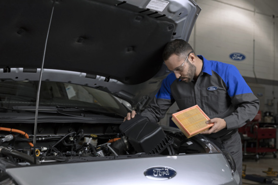 Ford technician checking air filter in silver Ford vehicle during routine maintenance service