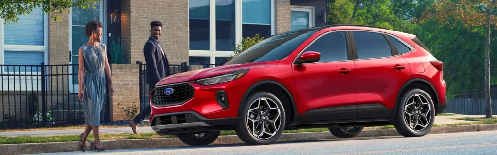 A red Ford Escape parked in front of a modern building with two people walking beside it.