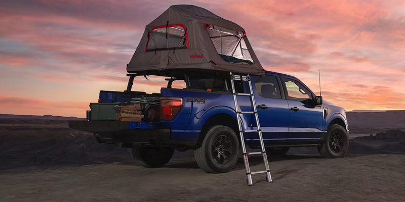 Pickup truck with a rooftop tent and ladder set up for camping at sunset.